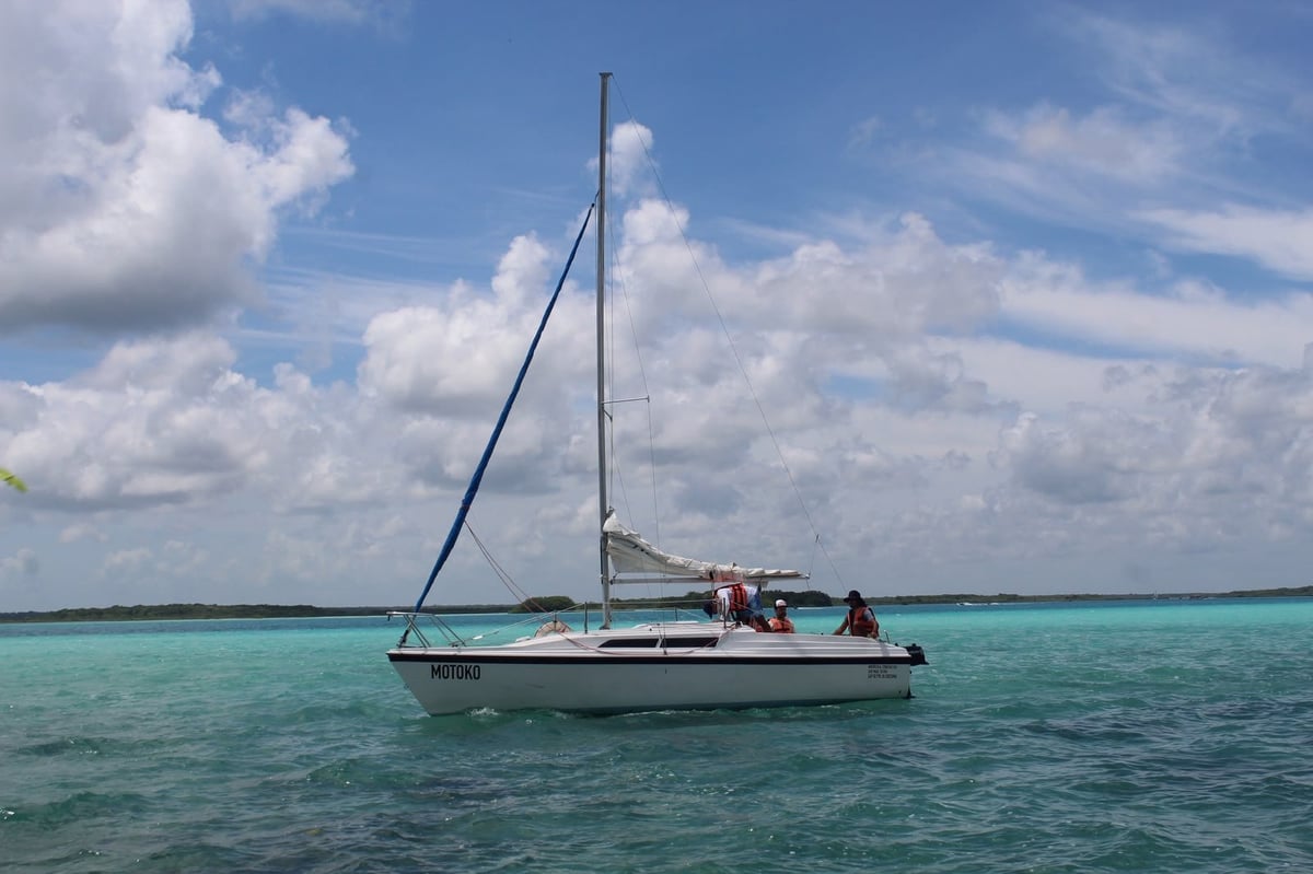 Velero anclado en las aguas turquesas de la Laguna de los Siete Colores con nubes blancas en el cielo azul