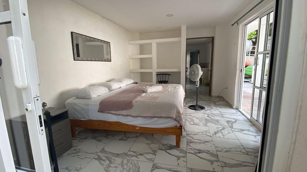 Recámara del departamento con cama matrimonial, sábanas blancas y puerta corrediza al exterior