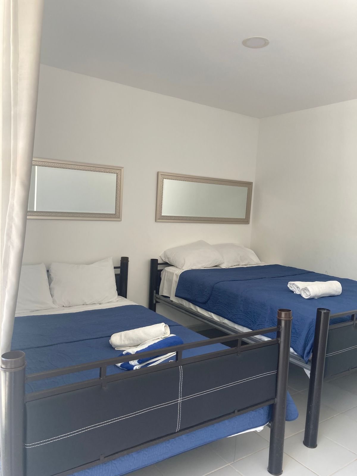 Habitación familiar con dos camas matrimoniales con colchas azules y espejos en la pared