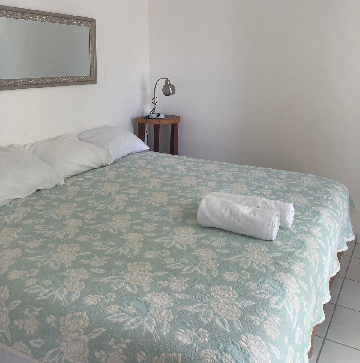 Habitación King con colcha verde estampada, almohadas blancas, toallas enrolladas y buró con lámpara