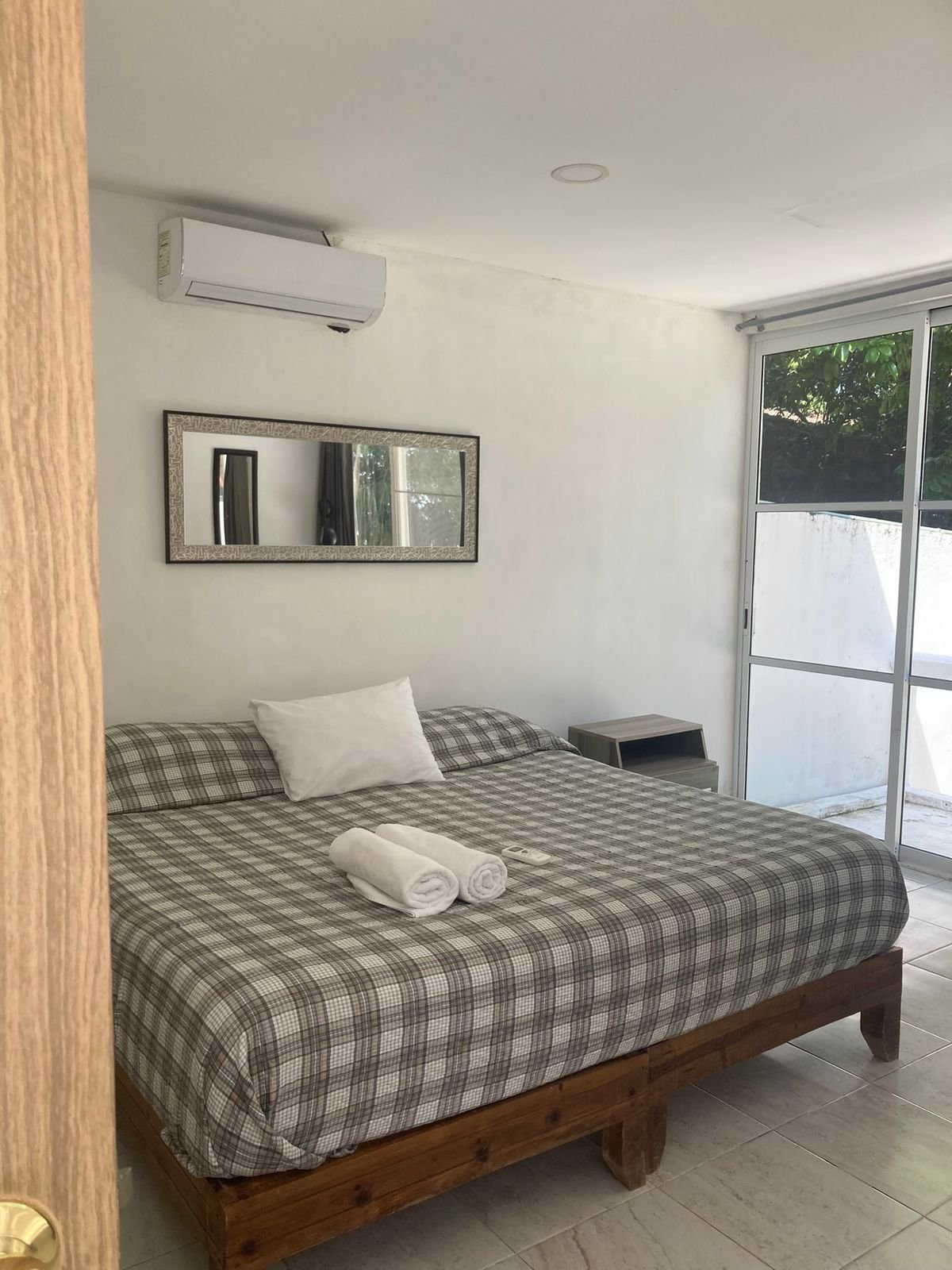 Recámara del departamento con cama de madera y puerta corrediza al exterior